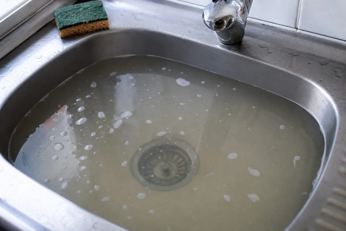 Évier de cuisine dont l&rsquo;eau stagne dans un appartement francilien, mousse de savon en surface