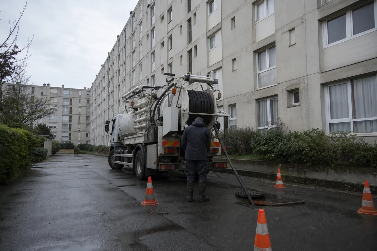 Camion d’hydrocurage stationné devant un immeuble de la banlieue sud parisienne, tuyau déroulé vers un regard de visite ouvert